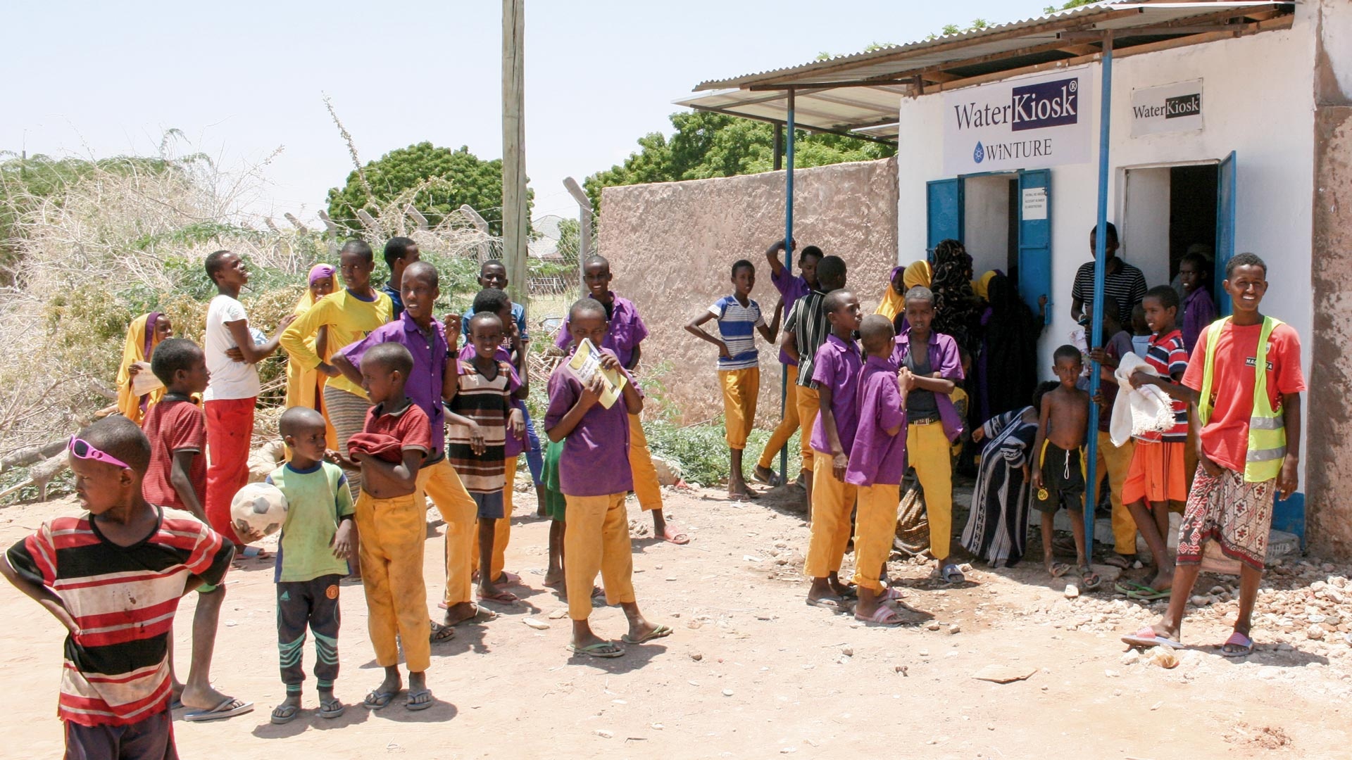A large group of Kenyan schoolboys stands in front of a WaterKiosk.