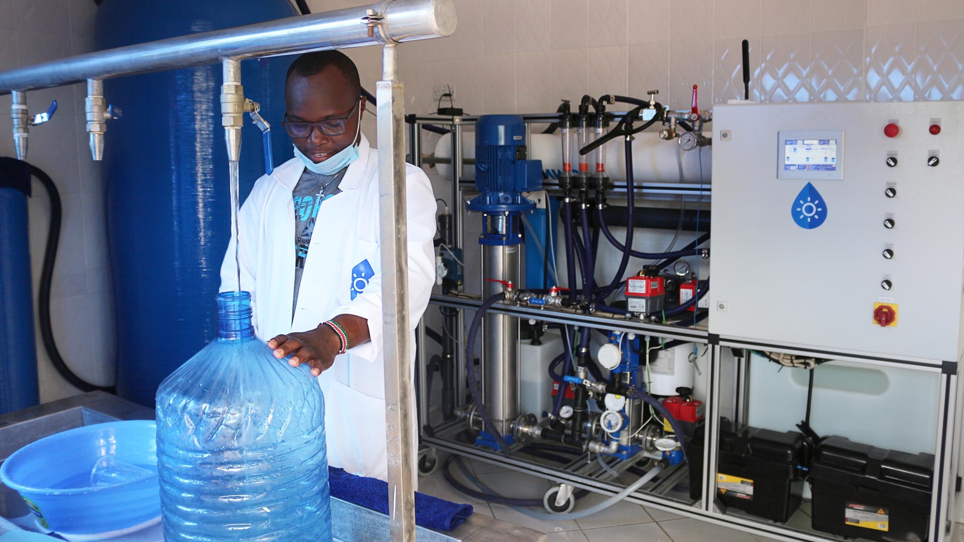 A Kenyan at the water treatment plant in a WaterKiosk fills drinking water into a large blue water bottle.