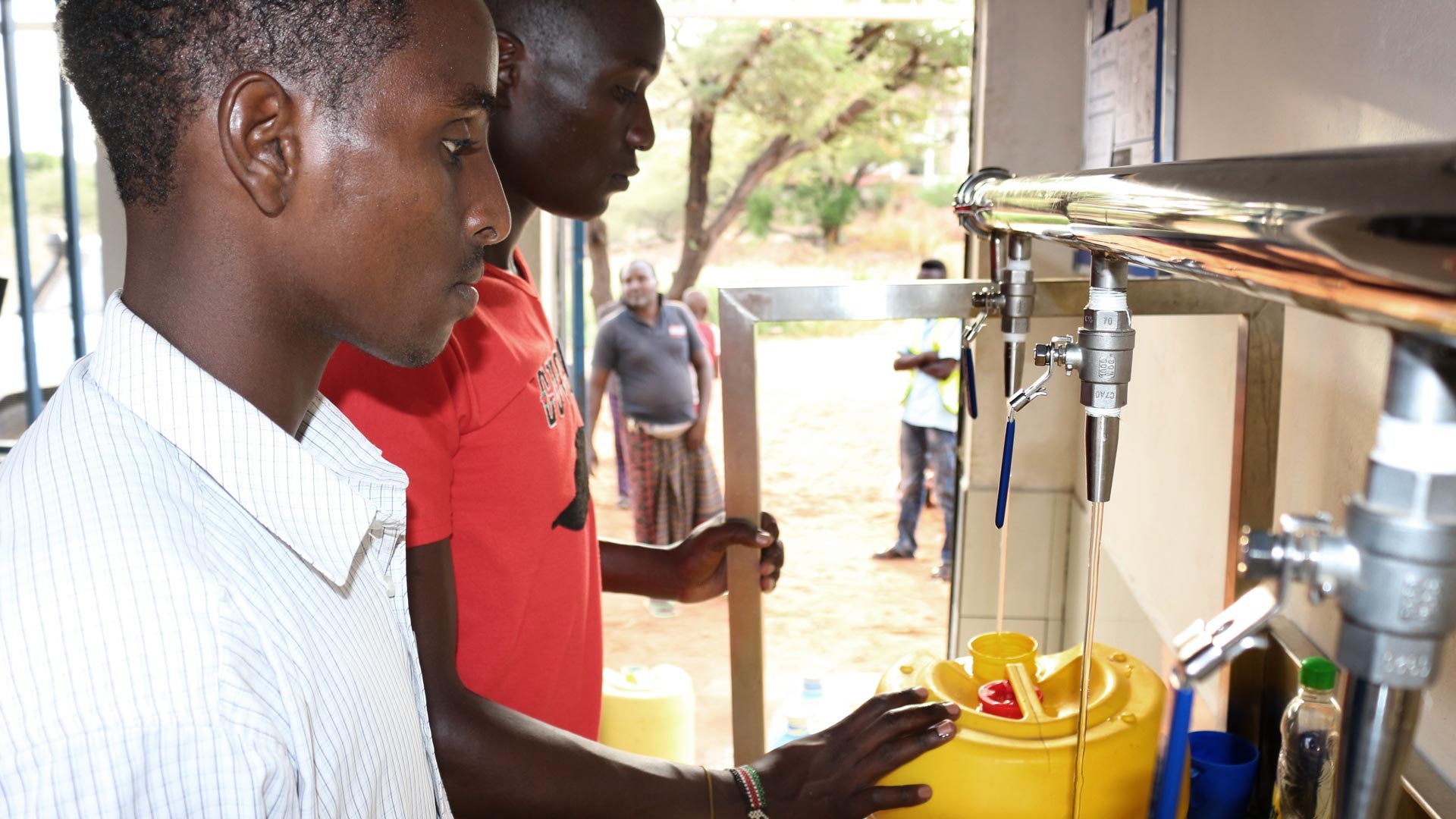 Zwei junge kenianische Männer füllen an einem WaterKiosk Trinkwasser ab