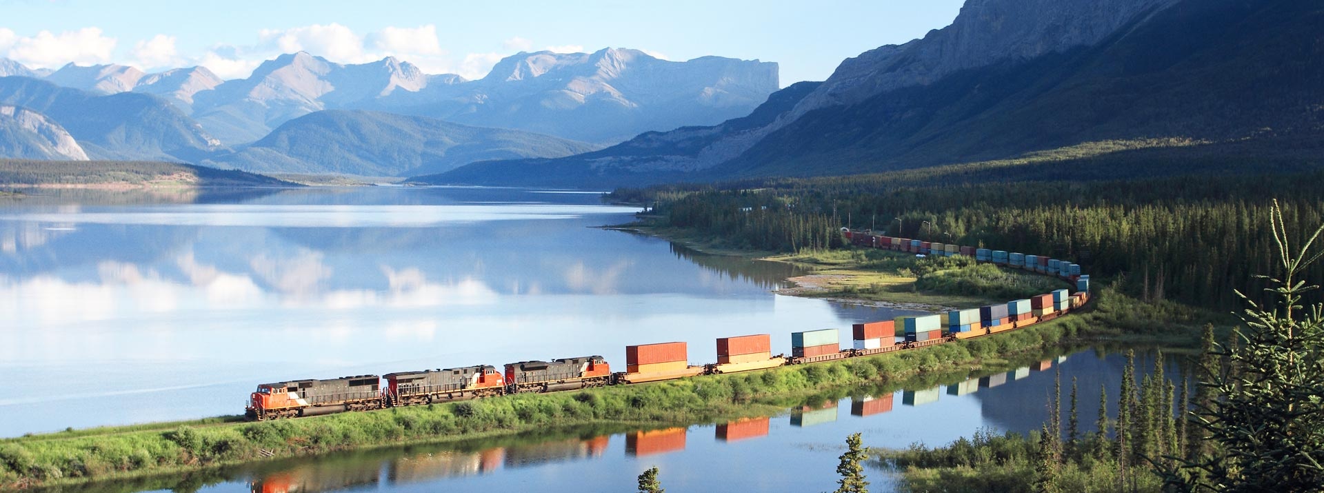 Freight-train-drives-infront-of-the-Brûlé-lake, Canada, with-mountains-in-the-background
