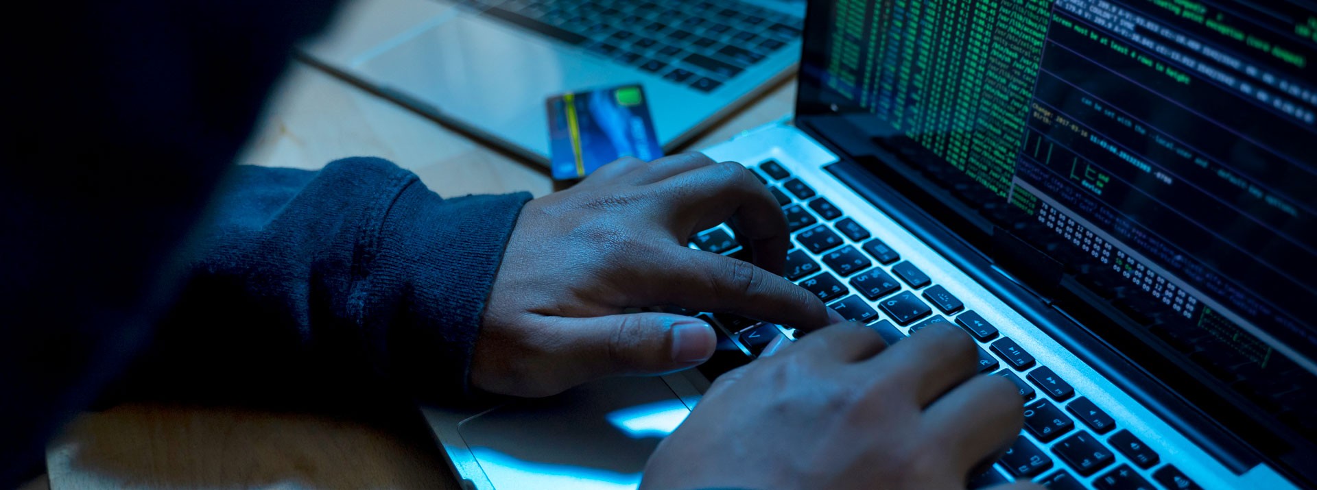 Hands on a laptop keyboard in a dark room, a credit card lying next to it