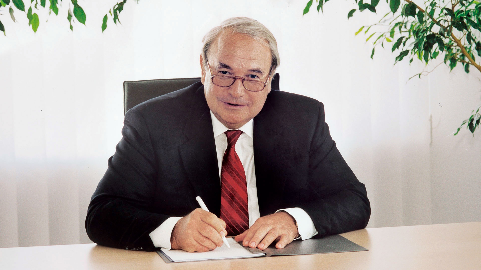 Heinz Hermann Thiele sitzt 1985 an seinem Schreibtisch und unterzeichnet Dokumente.