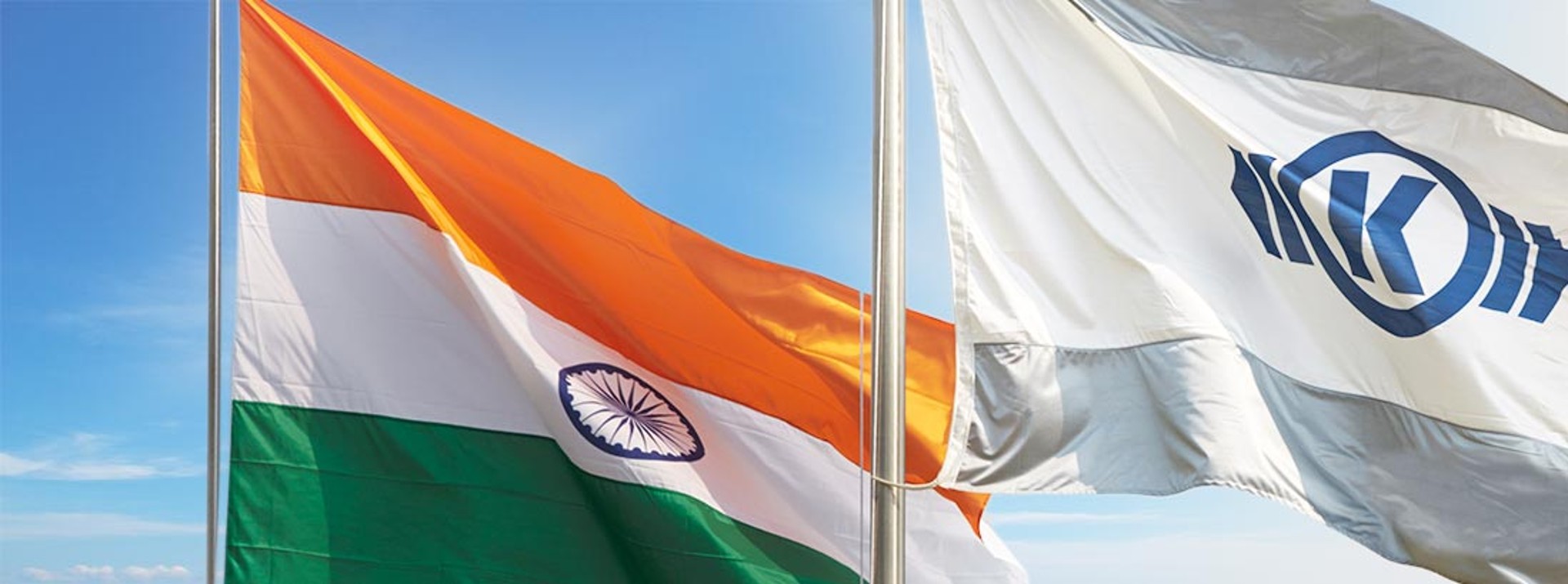 Two flags on the mast against a blue sky - one with the Indian flag on the left and one with the Knorr-Bremse logo on the right.