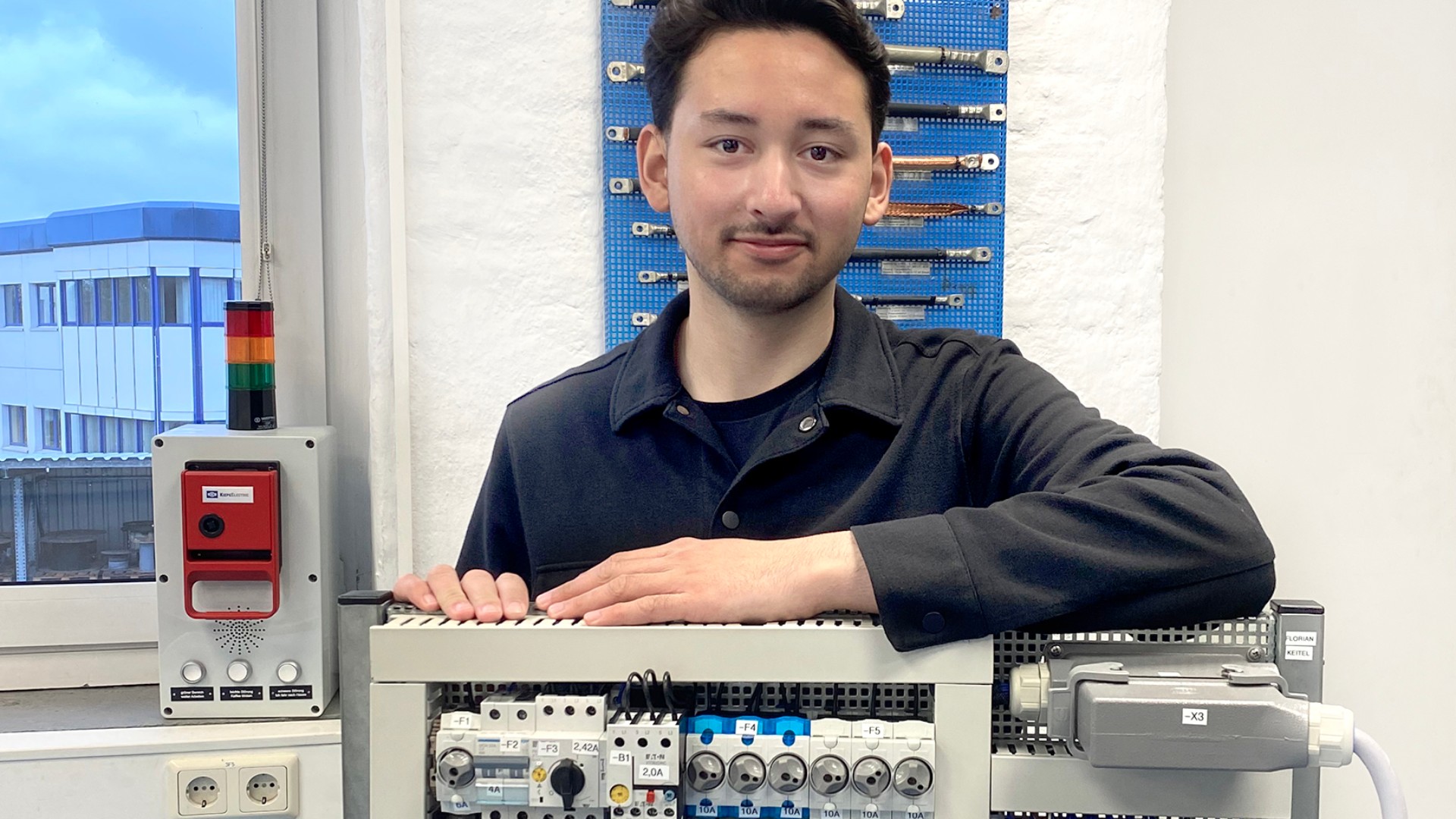 Apprentice Mike Ahrweiler from Kiepe Electric stands in front of an electronic construction kit in Kiepe's training workshop.