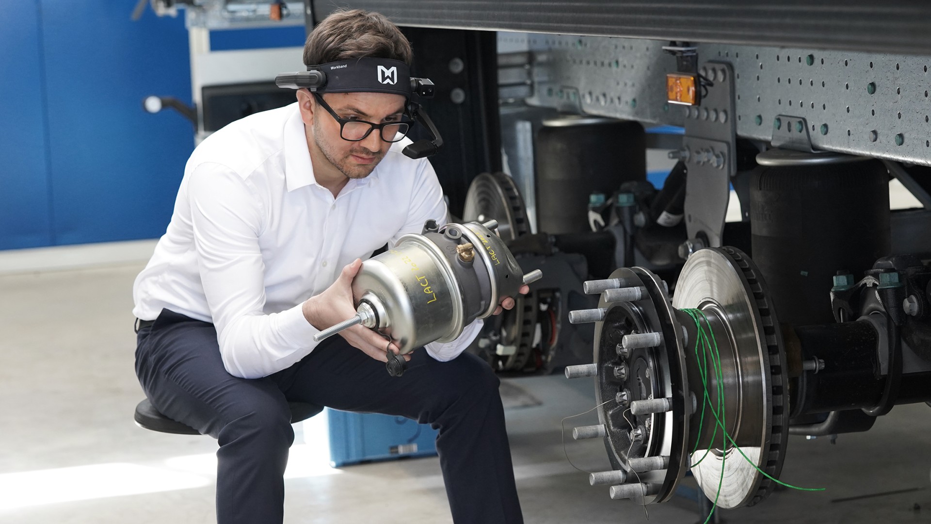In front of a truck in the workshop, a Knorr-Bremse employee uses AR glasses to look at a compressor.