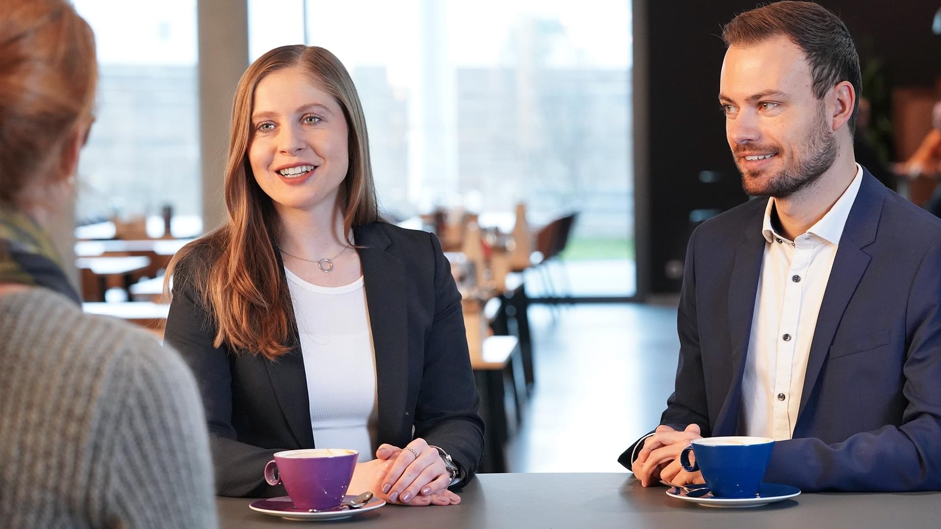 Die beiden Trainees Elina Steinke und Johannes Weth erzählen an einem Tisch in der Cafeteria am Knorr-Bremse Standort in München über ihre Erfahrungen mit dem MEP Traineeprpgramm.