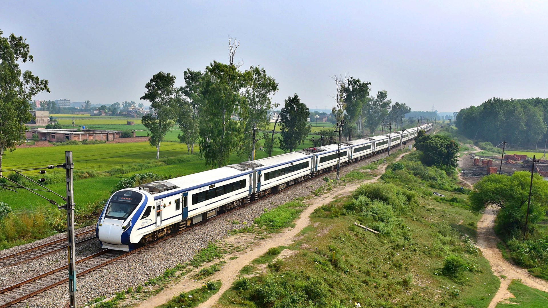 The new Indian intercity train Vande Bharat Express passes through Indian countryside outside a city.