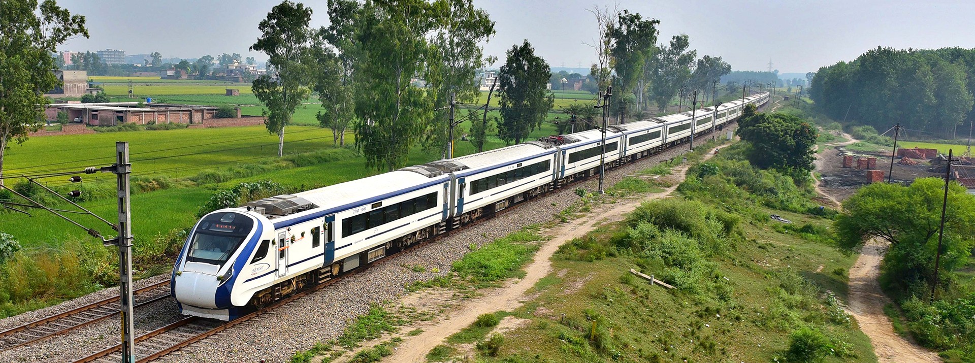 The new Indian intercity train Vande Bharat Express passes through Indian countryside outside a city.
