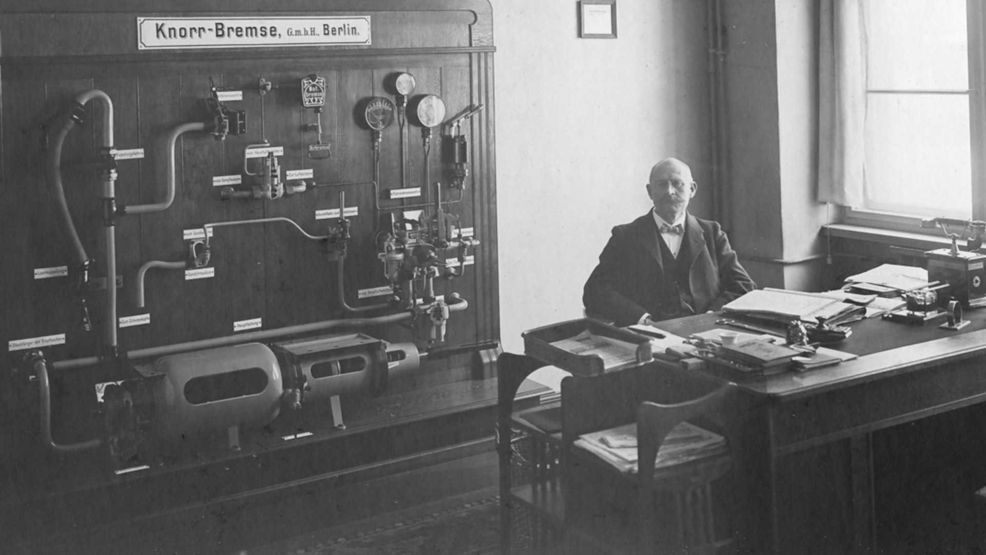 Historisches Büro mit technischem Aufbau einer Zug‑Druckluftbremse an der Wand und einer Person am Schreibtisch