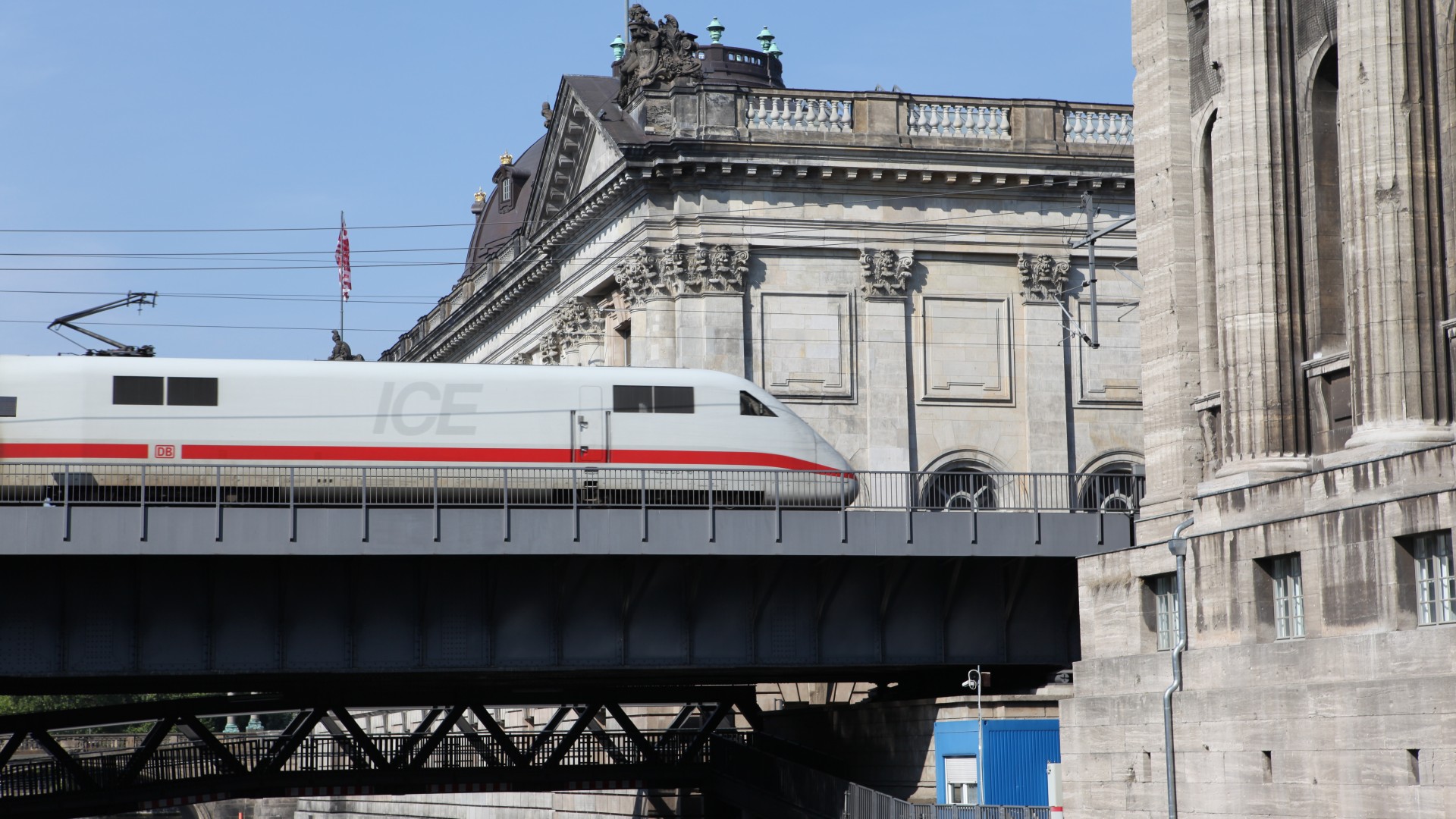 ICE high‑speed train crossing a bridge in front of historic architecture, symbolizing modern rail transport technology