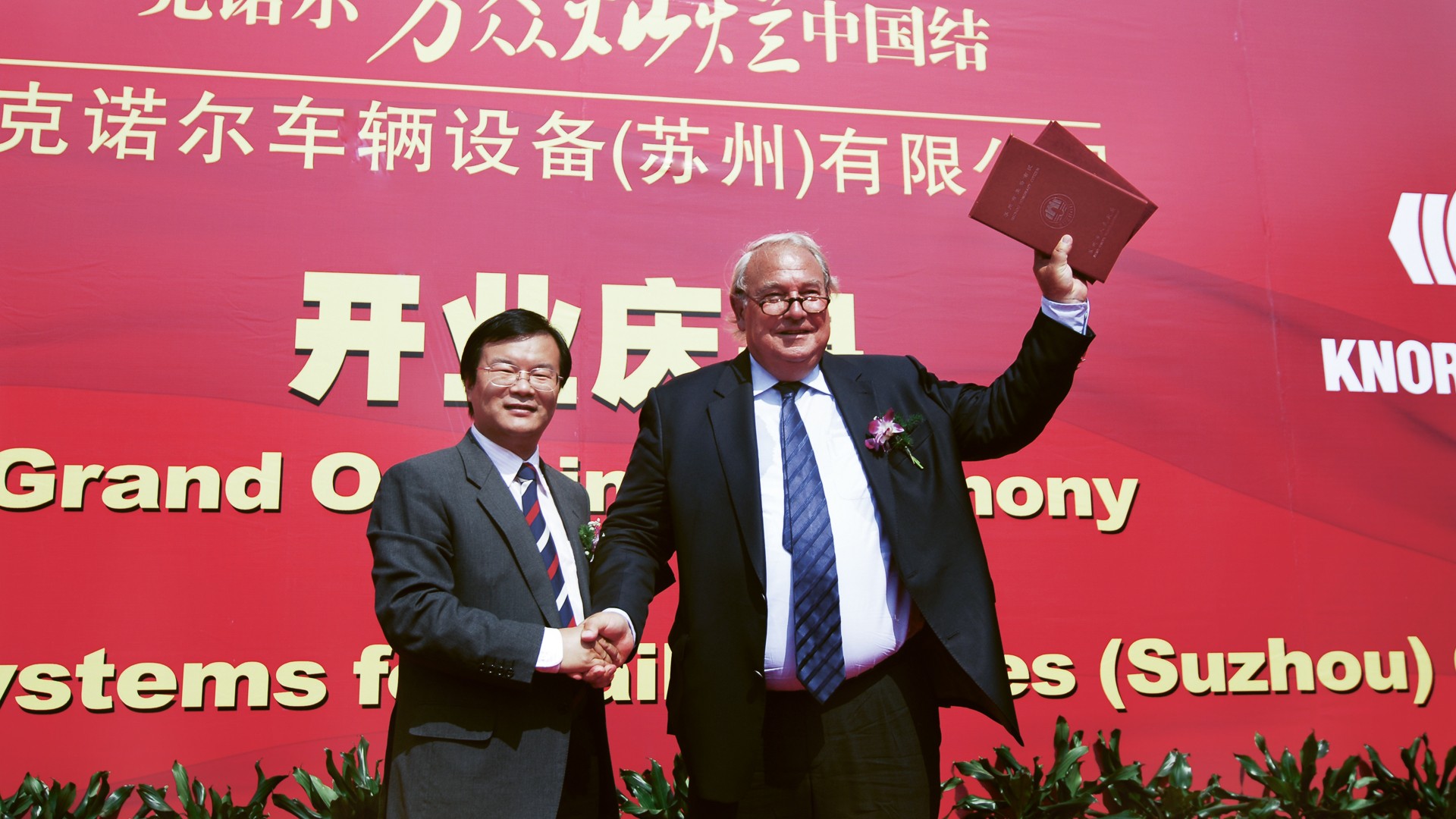 Eröffnungszeremonie eines Knorr‑Bremse Standorts in China mit Händedruck auf der Bühne