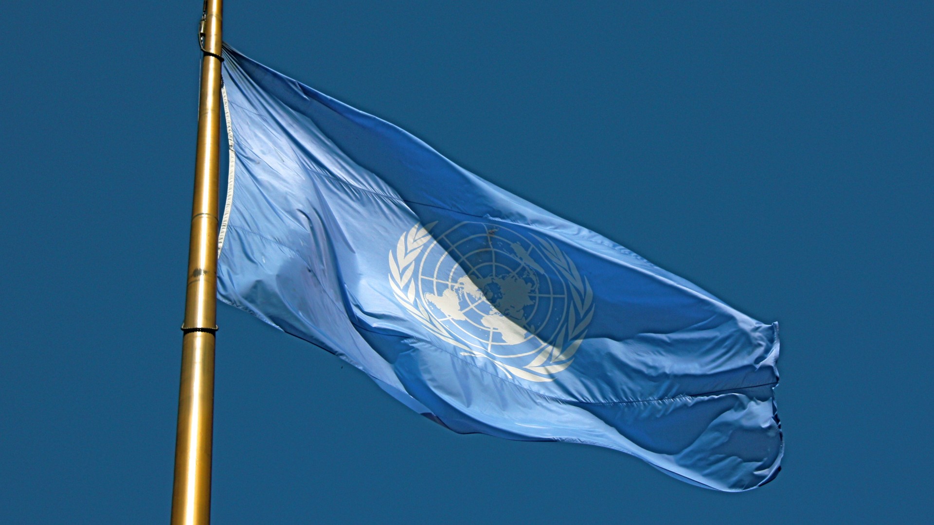 Flagge der Vereinten Nationen weht an einer Fahnenstange vor blauem Himmel