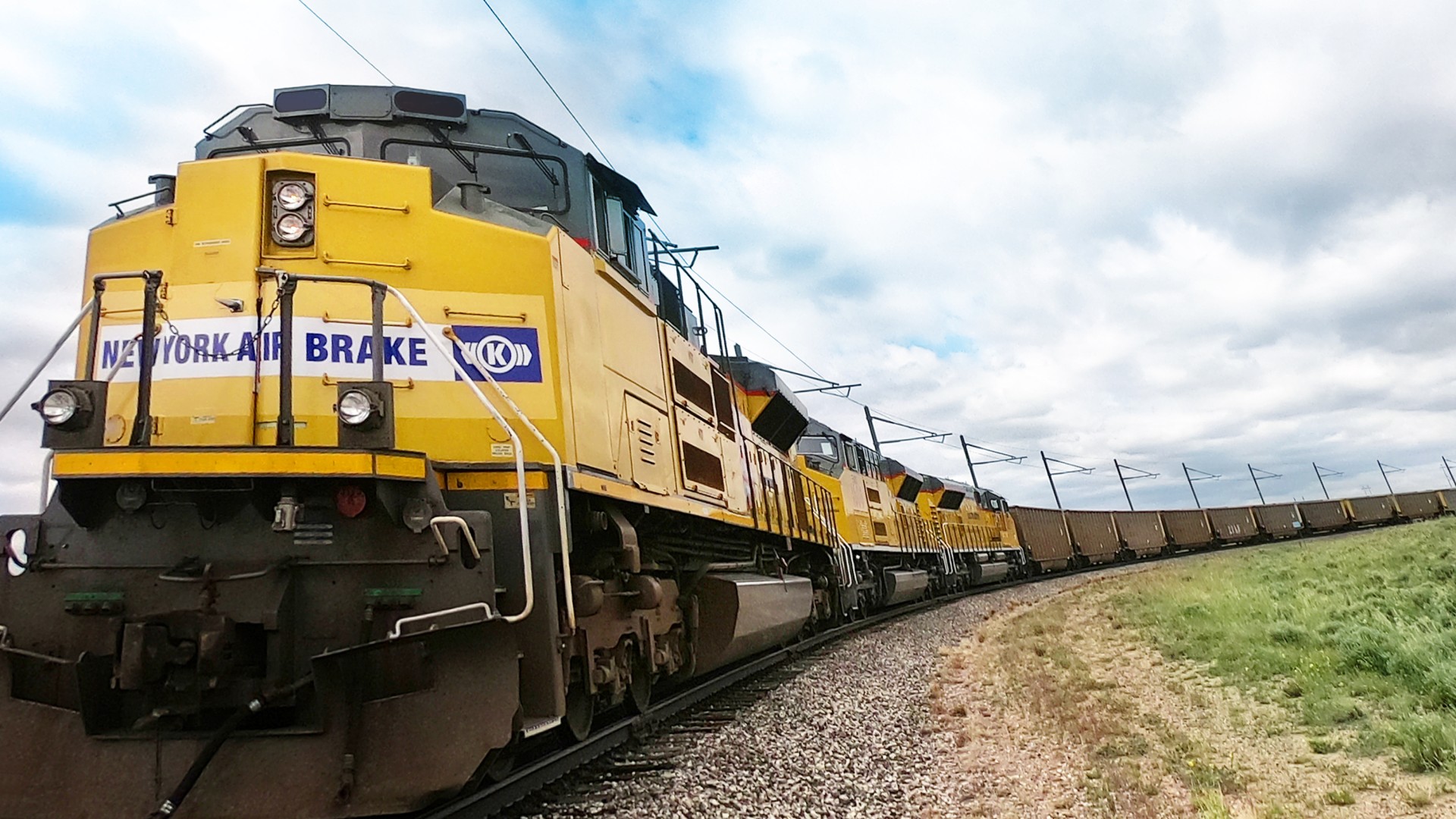 Gelber amerikanischer Güterzug mit einem New York Air Brake Logo vorne auf der Lokomotive auf einer kurvigen Bahnstrecke