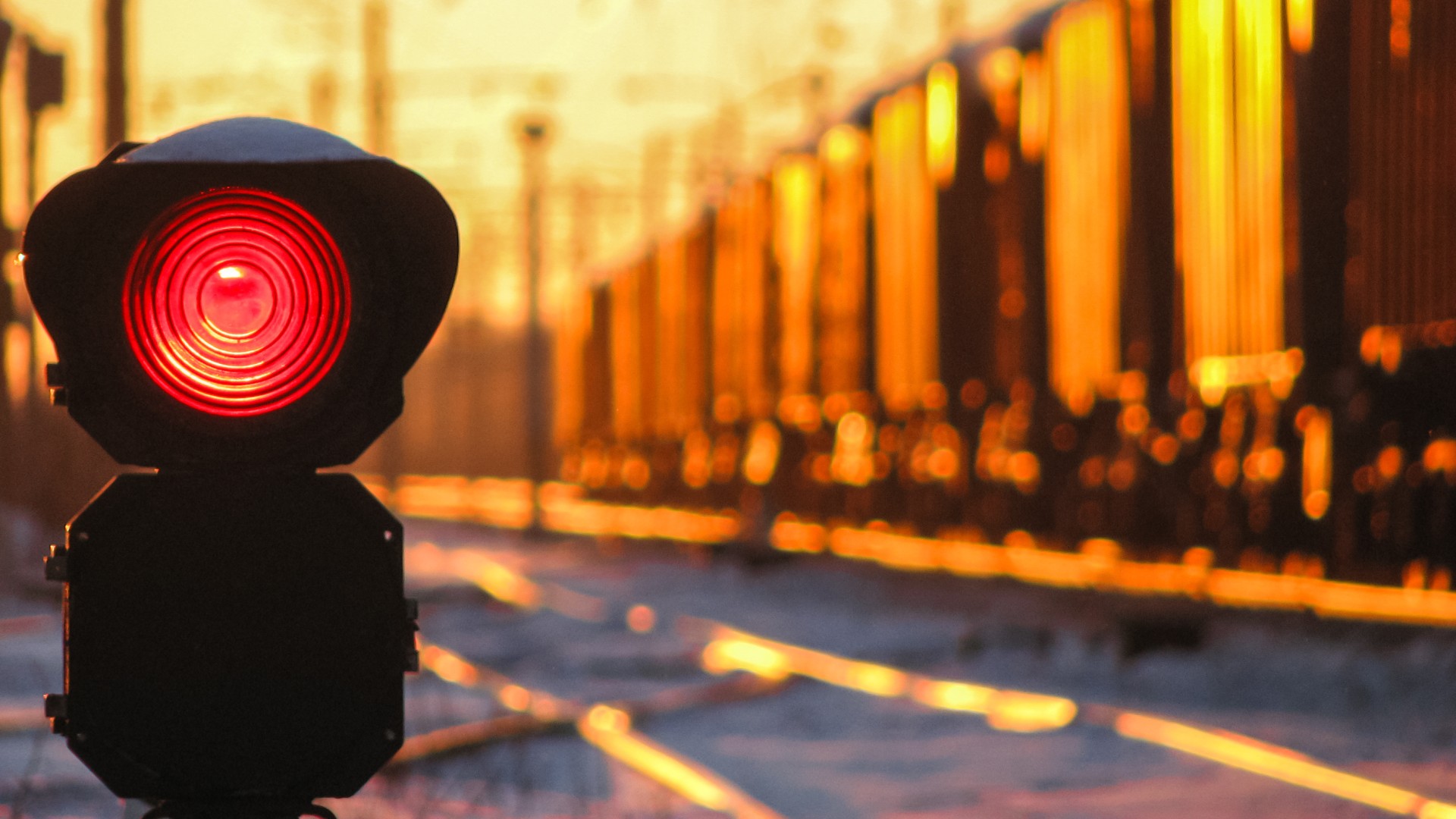 Rotes Eisenbahnsignal vor Güterwagen auf einer Gleisanlage im Abendlicht