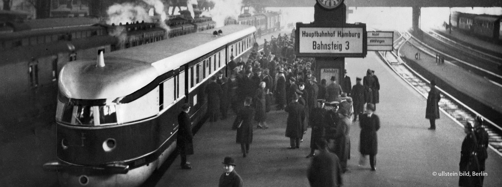 Historisches Schwarz-Weiß-Foto des Zugs ‚Fliegender Hamburger‘ bei der Einfahrt in den belebten Hamburger Hauptbahnhof.