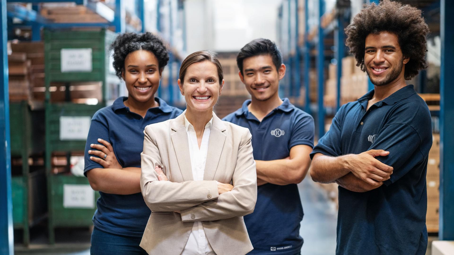 Diverse team of employees in an industrial setting with a female leader standing confidently in front, symbolizing modern leadership at Knorr‑Bremse