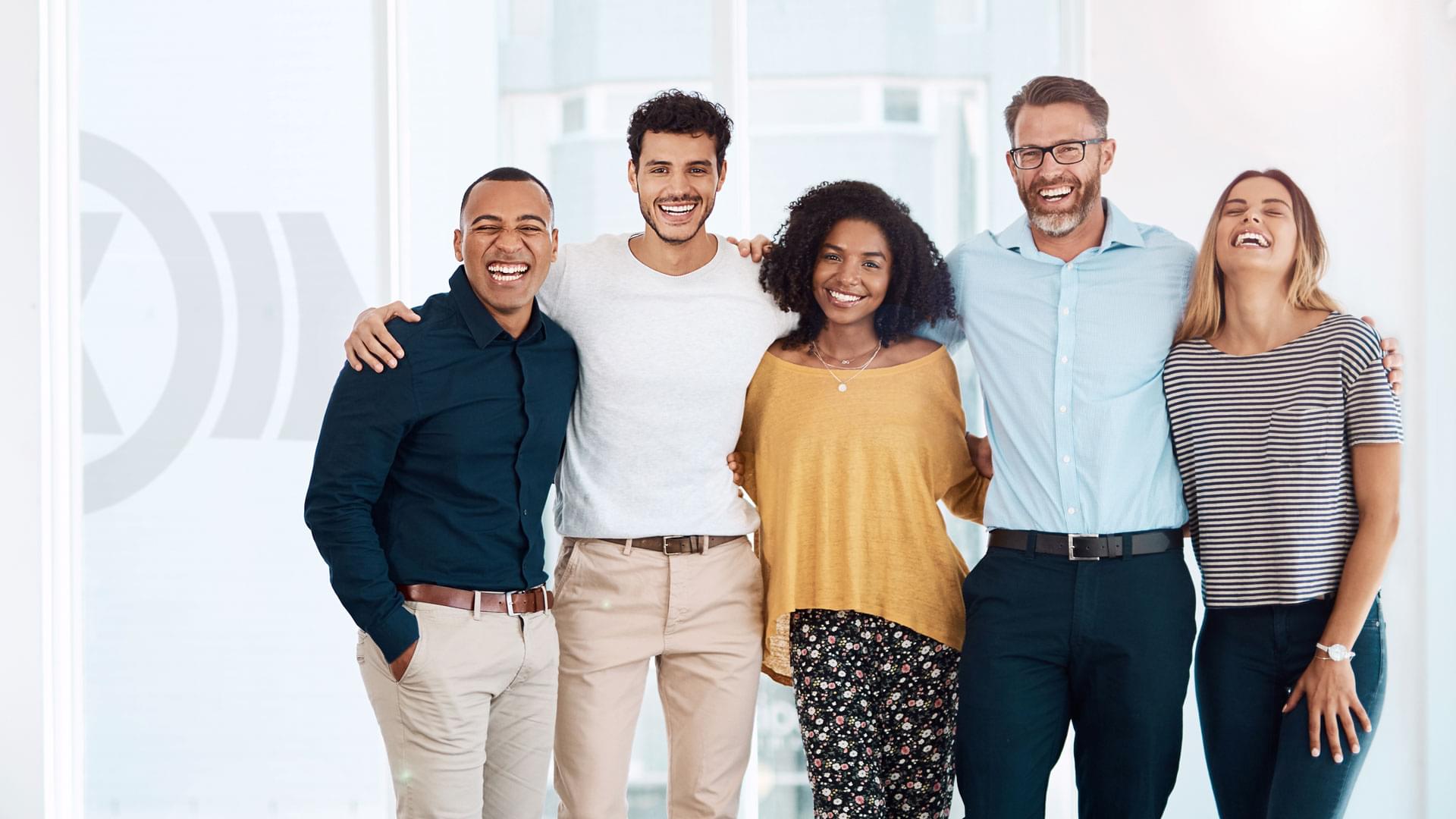 Diverse group of employees of different ages, genders and cultural backgrounds standing arm in arm, symbolizing team spirit and Knorr‑Bremse’s corporate culture