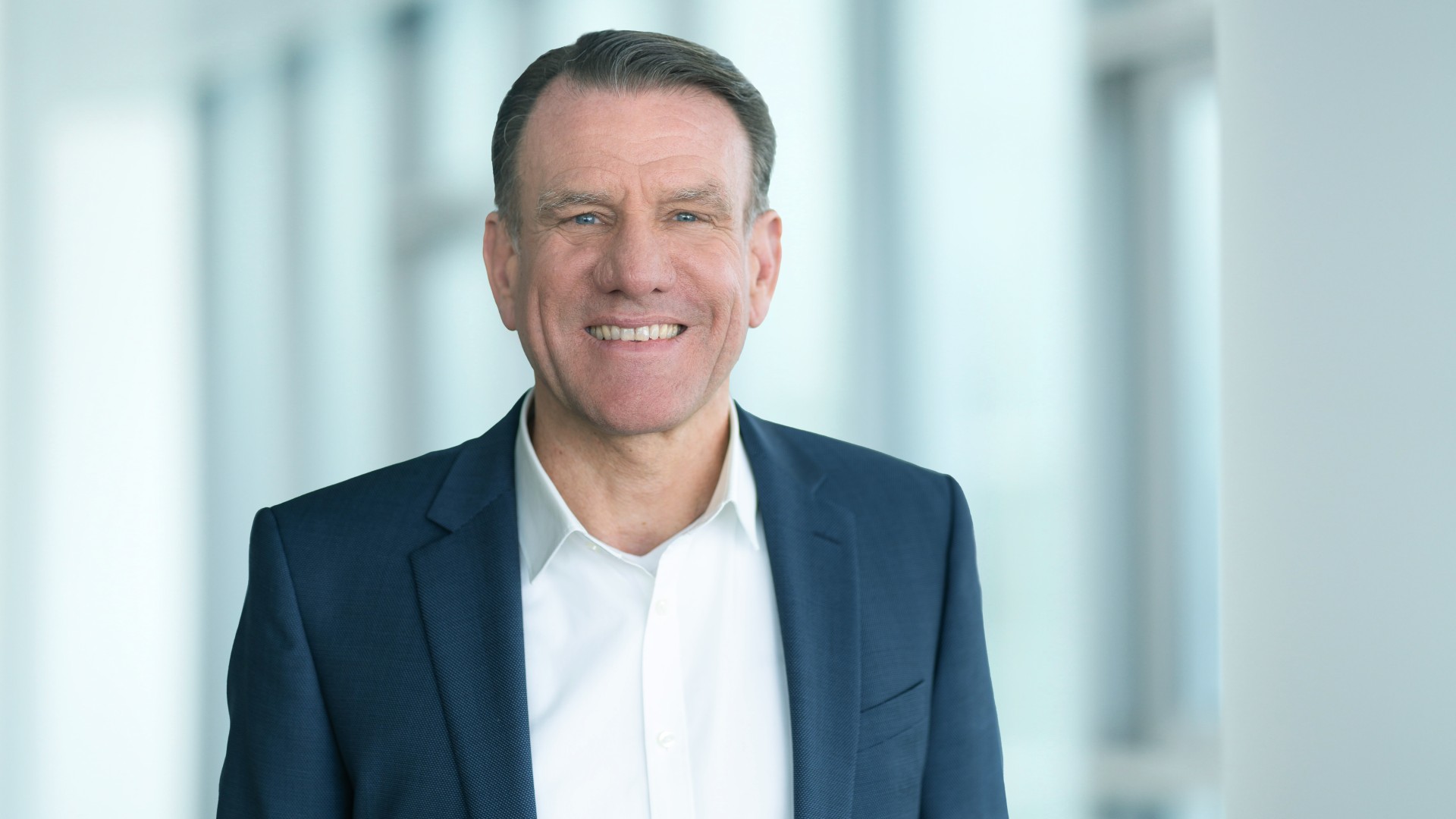 Porträtfoto eines Vorstandsmitglieds der Knorr‑Bremse AG mit Verantwortlichkeit für die Division Systeme für Nutzfahrzeuge, im Business‑Anzug vor einem modernen Büro-Hintergrund