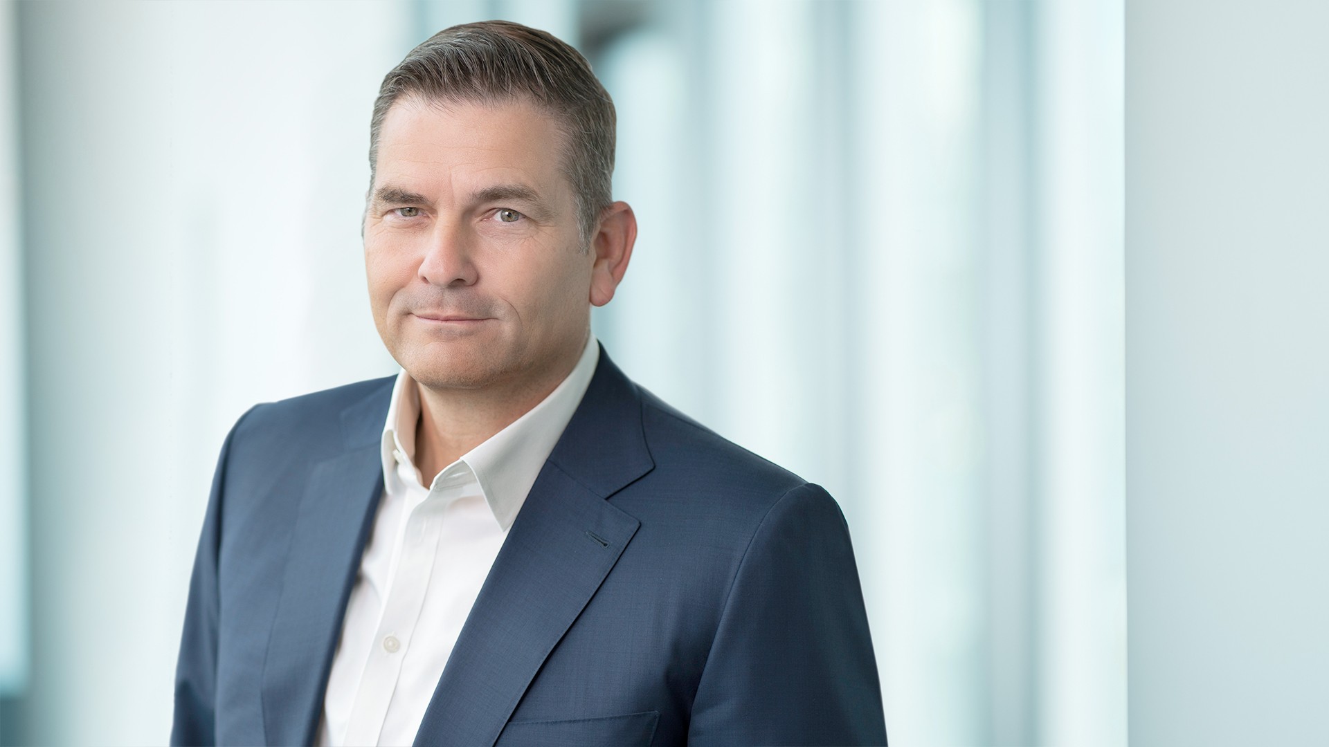 Portrait photo of the CEO of Knorr‑Bremse AG shown in a business suit against a modern office background