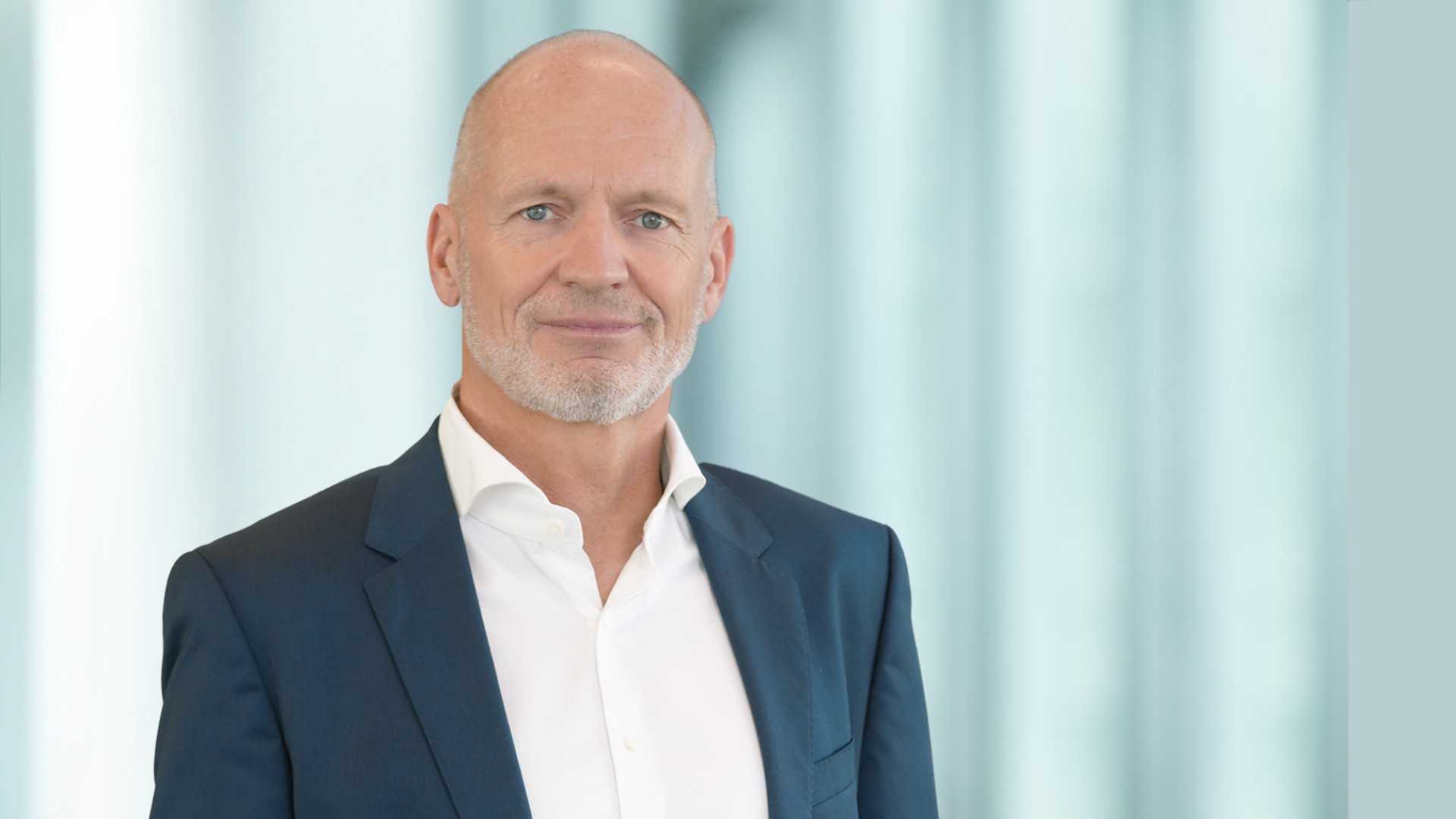 Portrait photo of a Knorr‑Bremse AG executive responsible for the Rail Vehicle Systems division, shown in a business suit against a modern office background