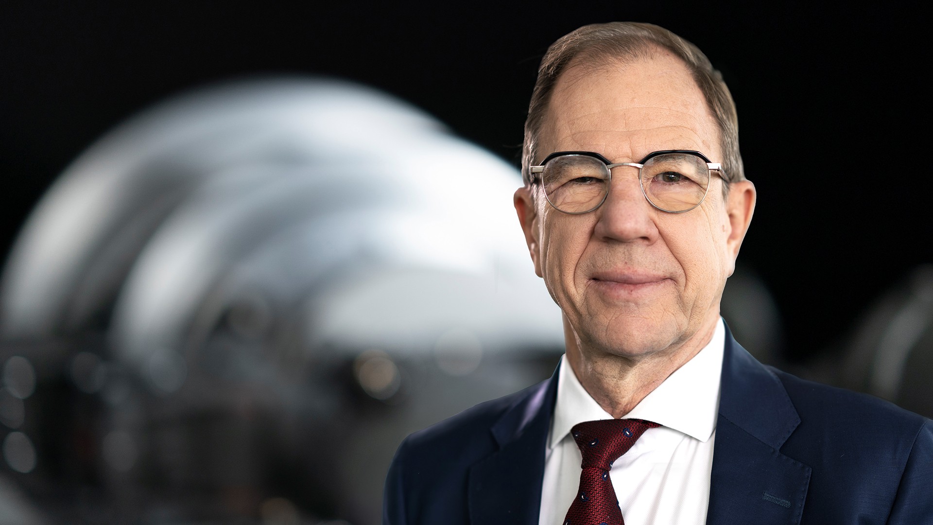 Business‑Portrait des Aufsichtsratsvorsitzenden der Knorr‑Bremse AG vor industrieller Maschinenkomponente