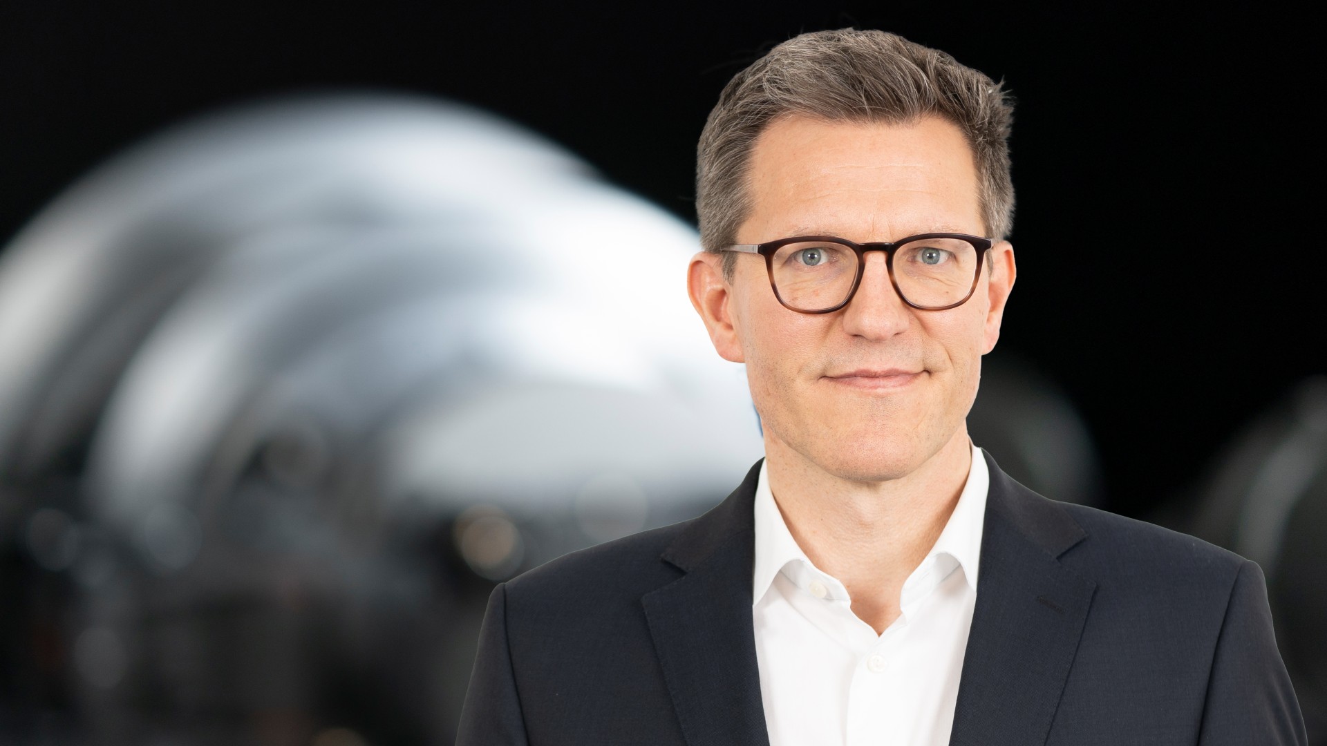 Business‑Portrait eines Aufsichtsratsmitglieds der Knorr‑Bremse AG vor industrieller Maschinenkomponente
