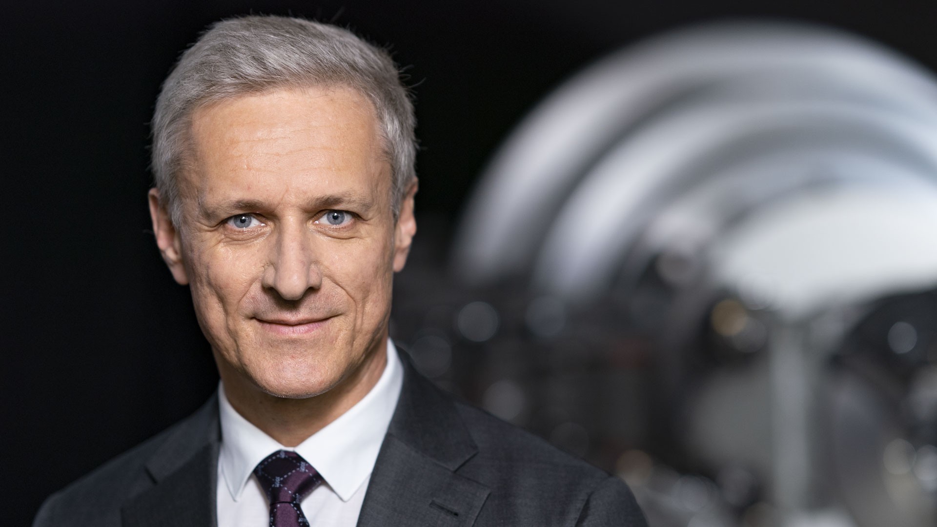 Business portrait of a supervisory board member of Knorr-Bremse AG in front of an industrial machinery component