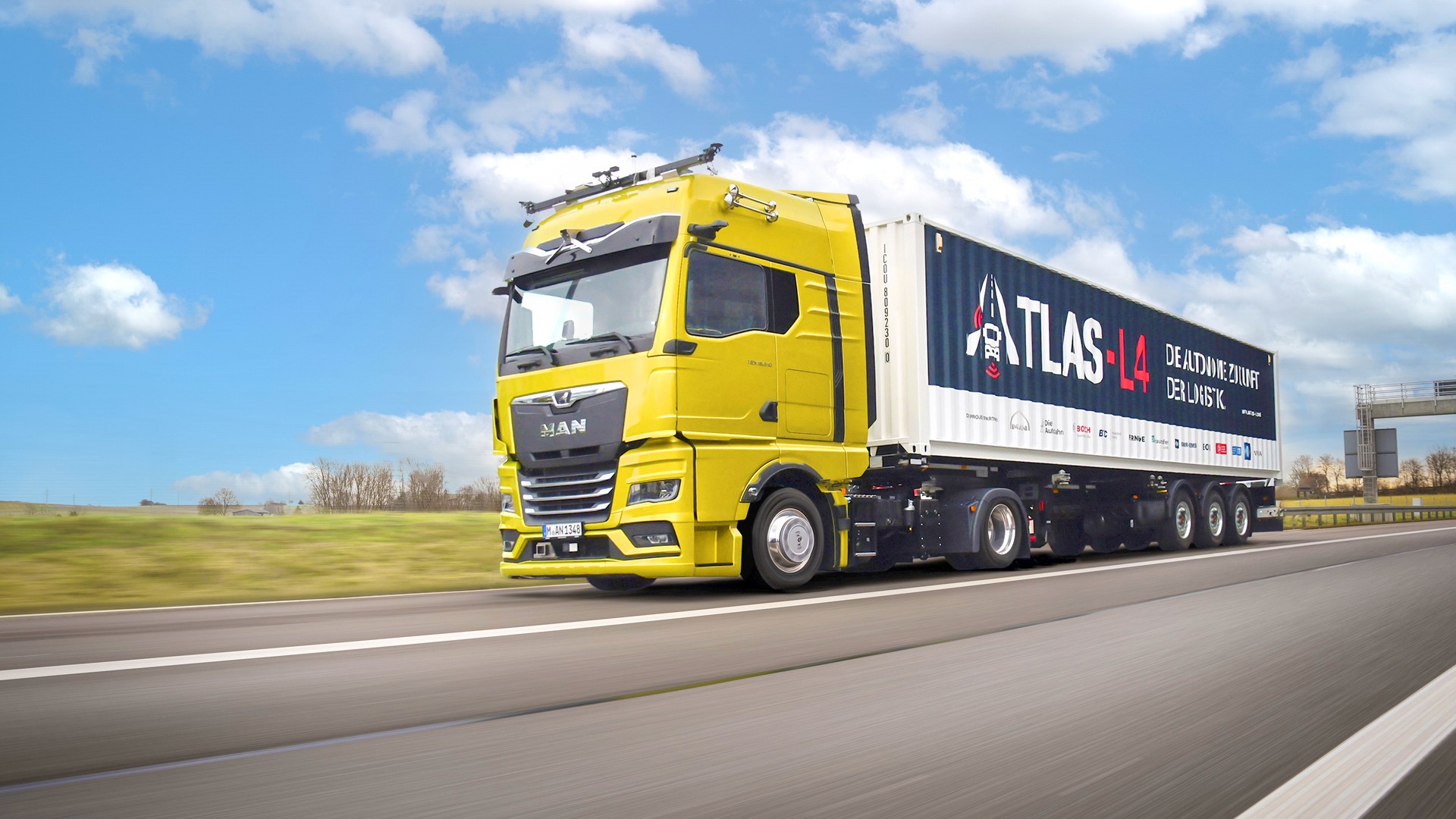 Ein MAN-Lkw mit Anhänger fährt auf der Autobahn. Auf dem Anhänger ist groß ATLAS-L4 aufgedruckt und die Logos aller Partner des Projekts.