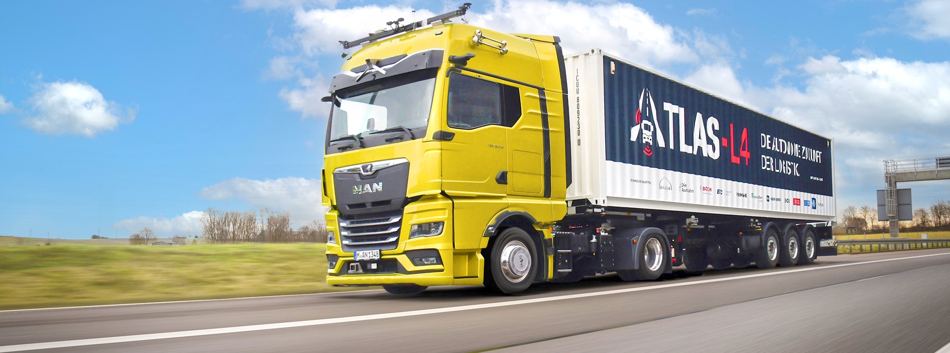 Ein MAN-Lkw mit Anhänger fährt auf der Autobahn. Auf dem Anhänger ist groß ATLAS-L4 aufgedruckt und die Logos aller Partner des Projekts.