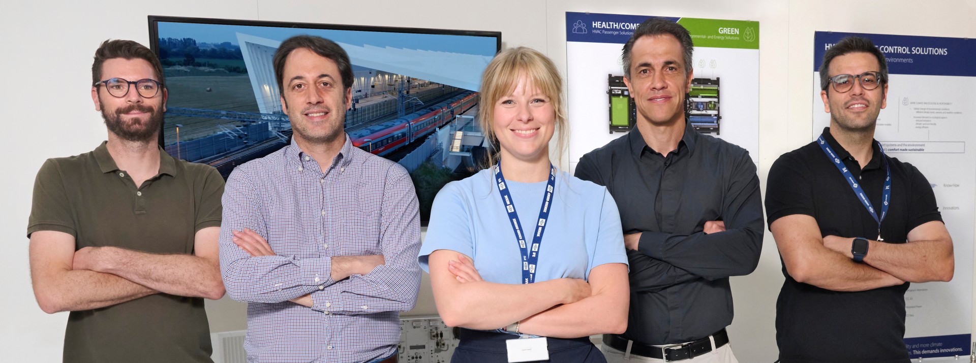 Laura Hajek steht mit ihren Kollegen aus dem Projektteam vor einer Plakat- und Bildschirmwand im Knorr-Bremse Werk in Getafe, Spanien.