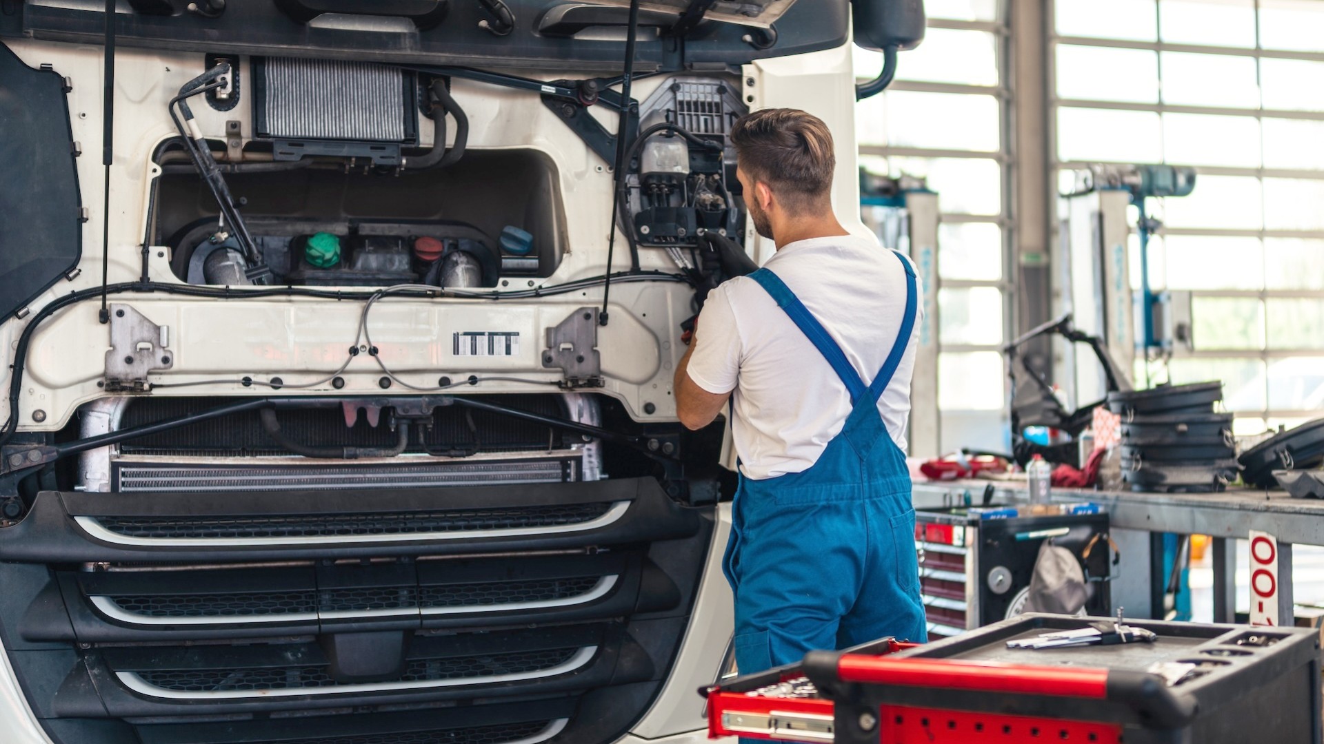 Ein Werkstattmitarbeiter arbeitet in einer Lkw-Werkstatt am geöffneten Kühlergrill einer Lkw-Sattelzugmaschine.