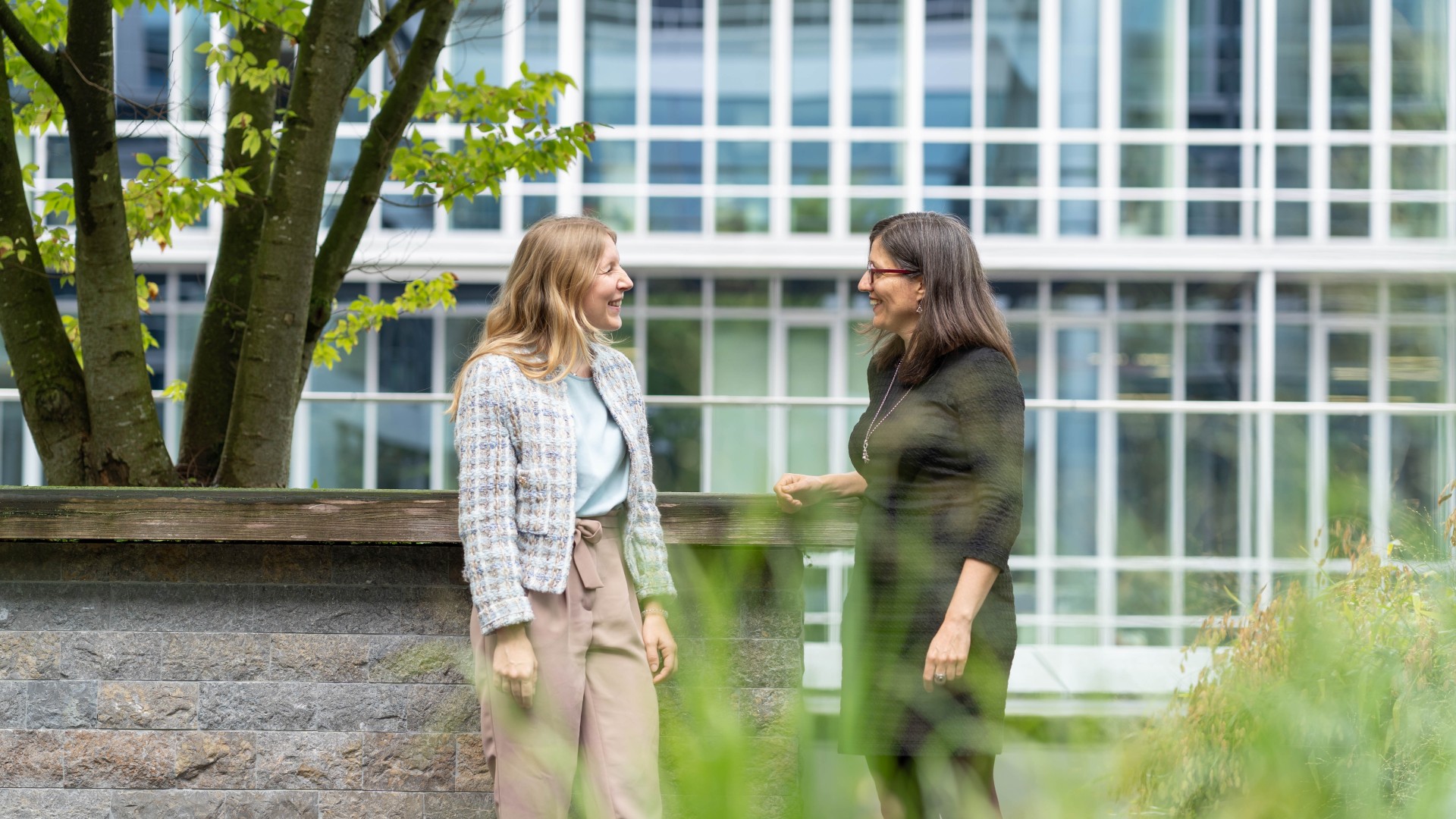 Two employees who lead the Generations@KB network talking outdoors near an office building, surrounded by greenery and modern architecture