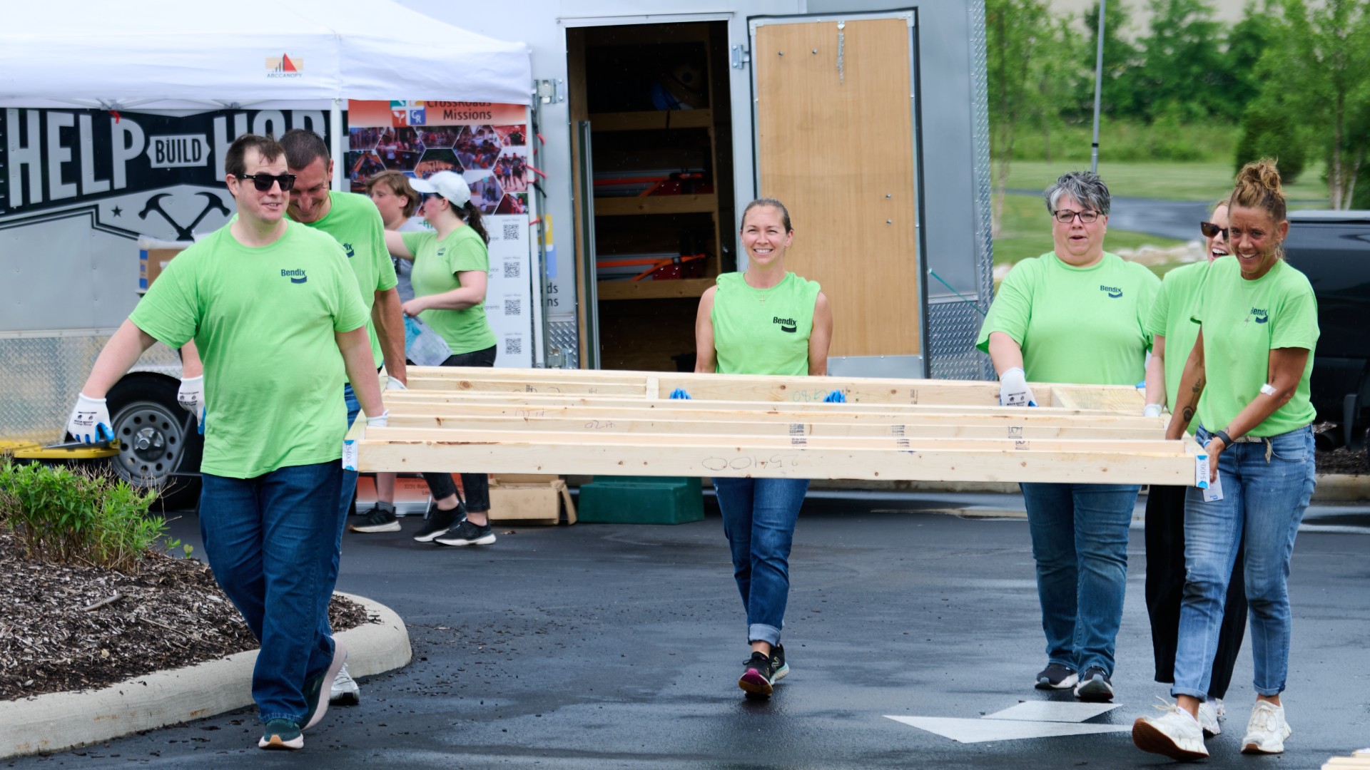 Bendix employees jointly carry the frame of a wall element for homes for families in need