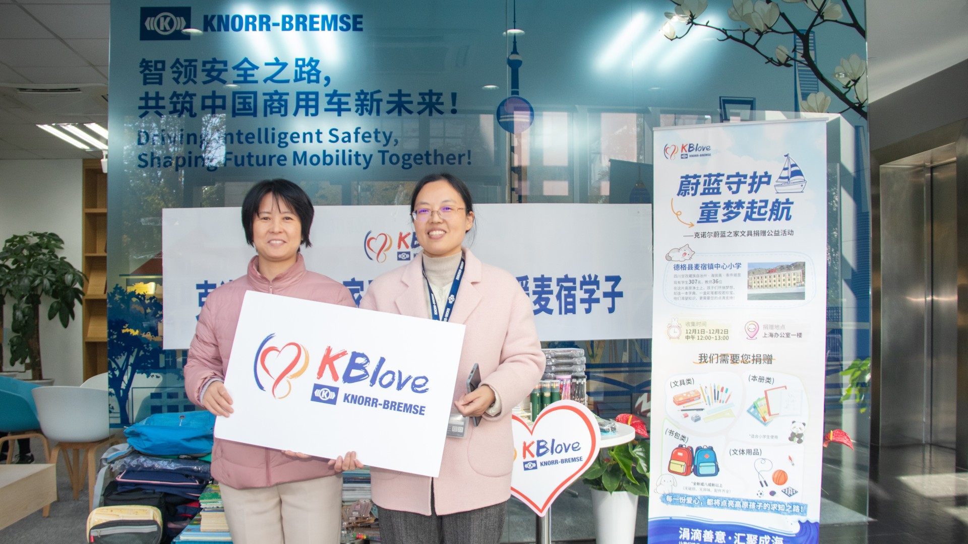 Employees of Knorr‑Bremse Shanghai stand in front of a table with collected school supplies to help provide children in a remote region of China with access to education