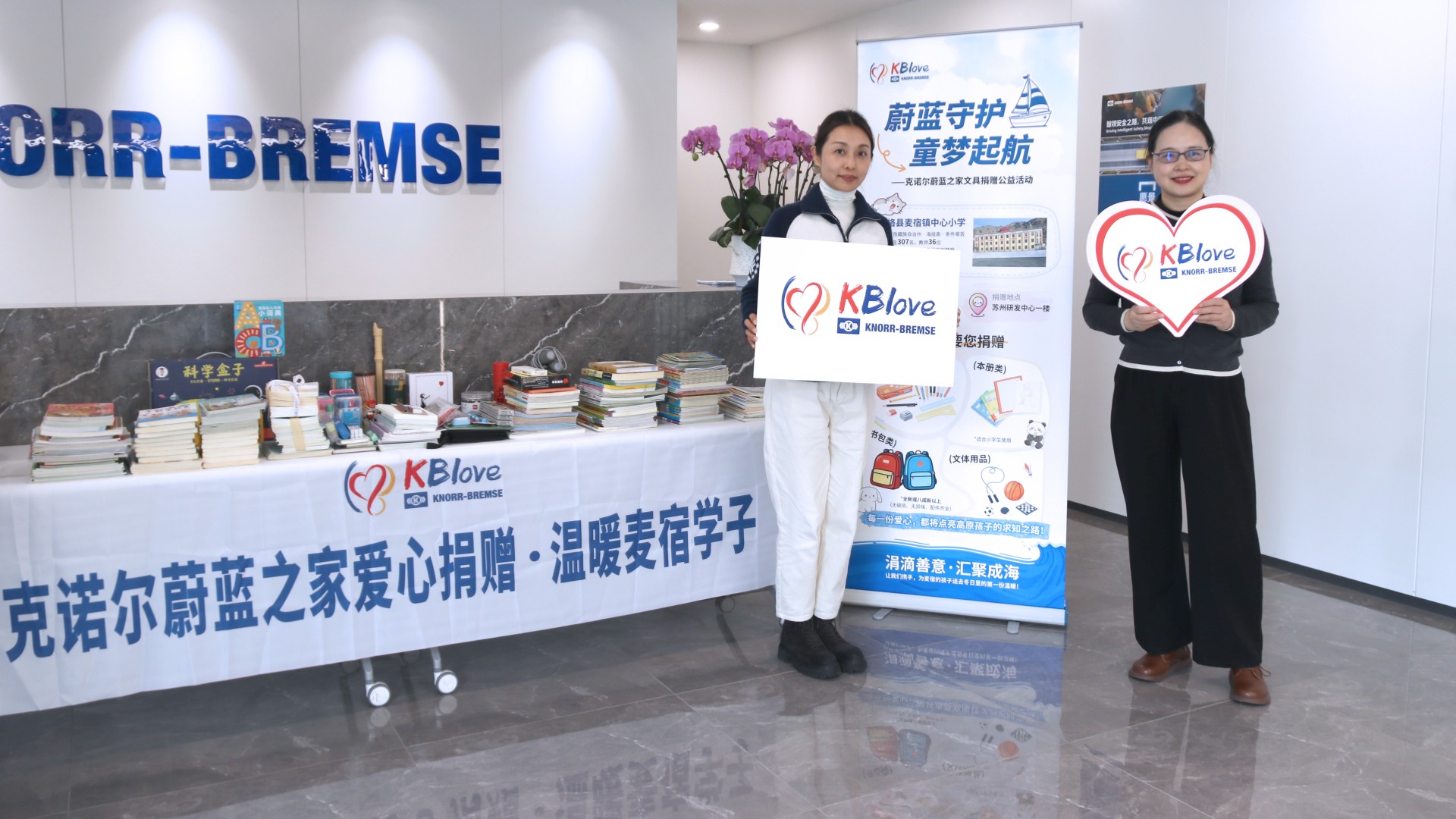 Employees from Knorr-Bremse Suzhou stand in front of a table with donated books and school supplies for primary school students in a remote region of China