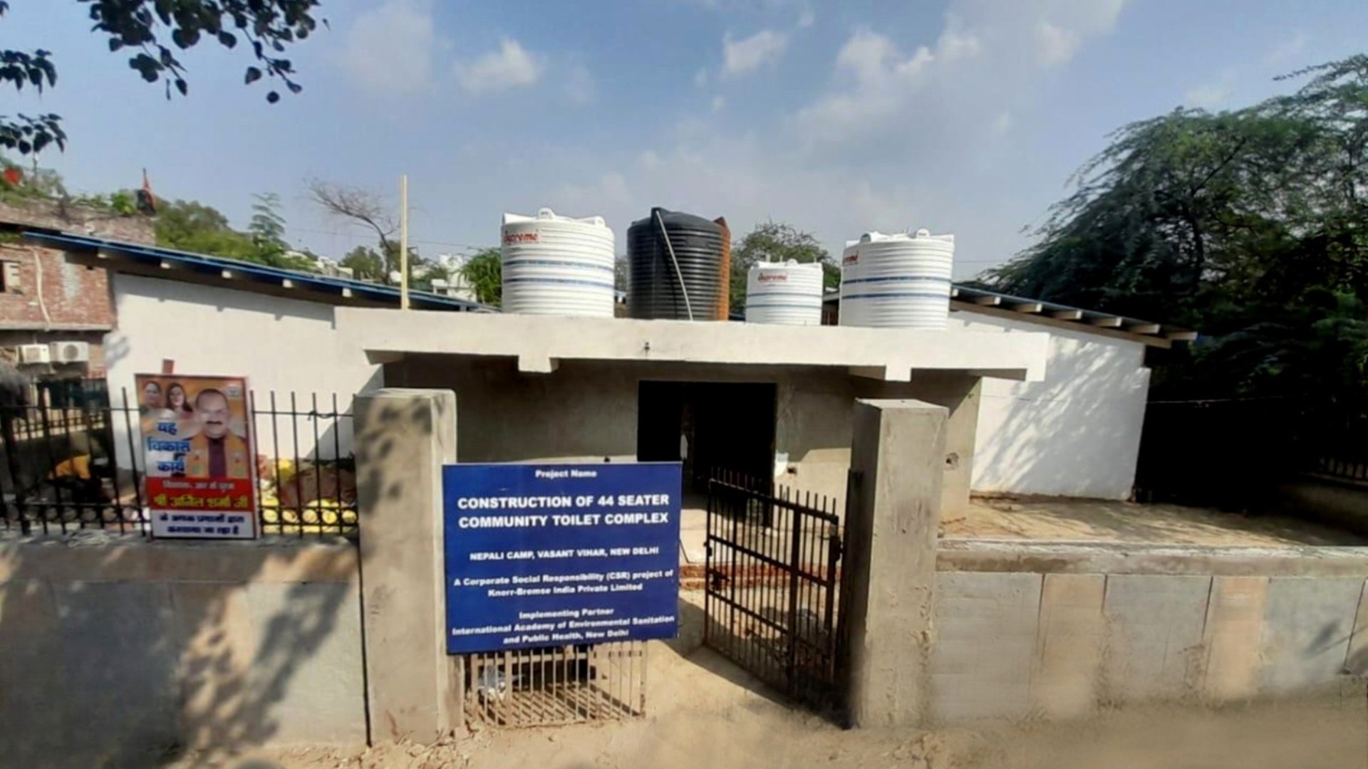 Construction of a community toilet complex with 44 seats for the Nepali Camp community in Delhi, shown with entrance gate and project information sign