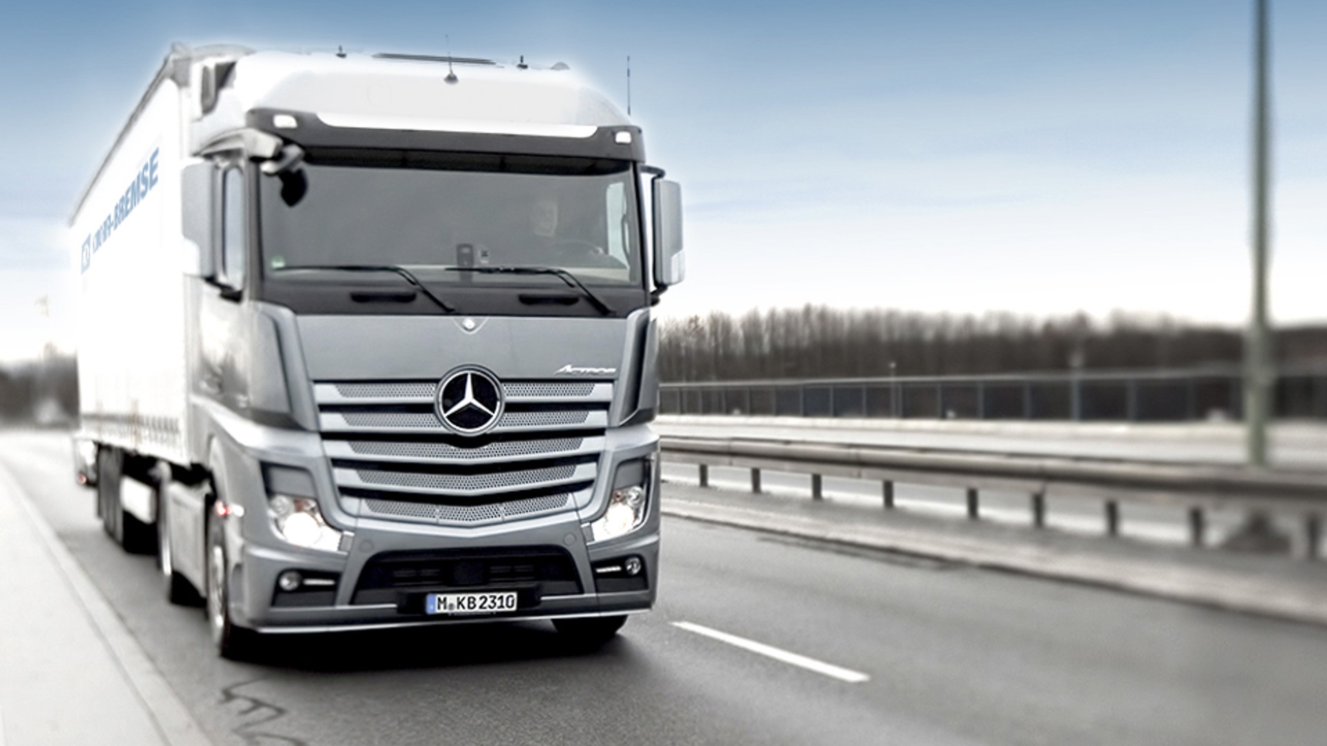 A Mercedes Actros truck with a Knorr‑Bremse logo on the side curtain driving on an empty two‑lane road – application area of the Knorr‑Bremse Truck Division