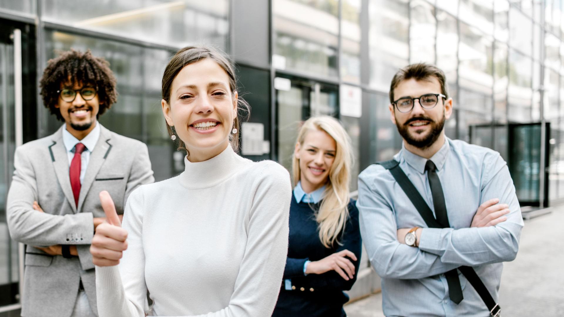 Mitarbeitende in Business‑Kleidung als Team vor modernem Bürogebäude