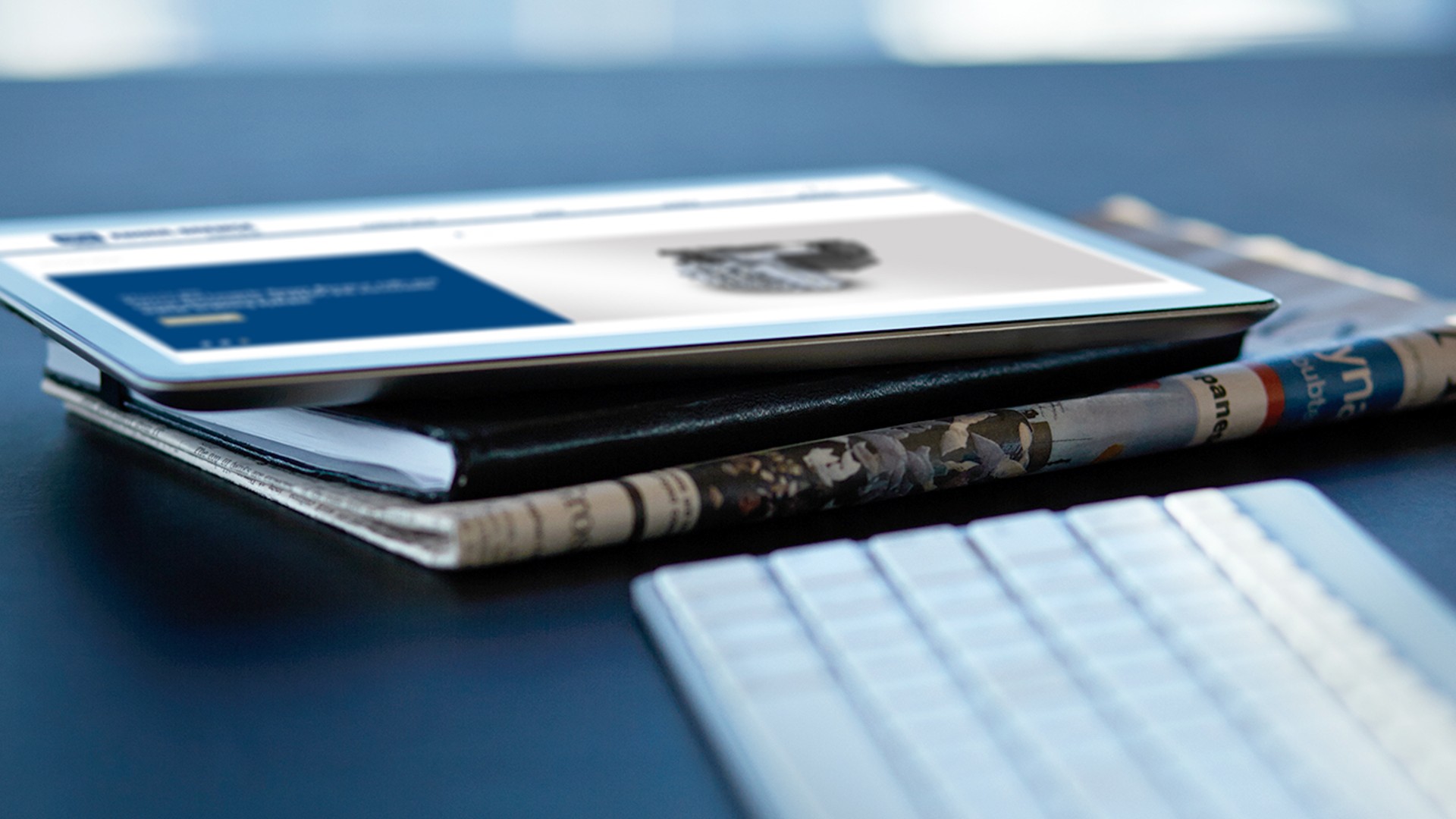 Workspace with keyboard, newspaper, notebook and tablet in a close‑up view